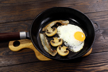 Breakfast. Frying pan with bacon,eggs and mushrooms on a wooden table.