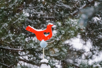Snow accumulation on red bird cutout with heart during snowstorm