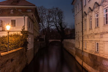 Fototapeta na wymiar A bridge and old palaces on the sides of a water canal in Prague at night