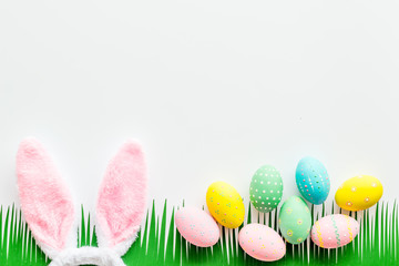 Easter concept. Eggs, Bunny's ears and grass on white background top-down copy space