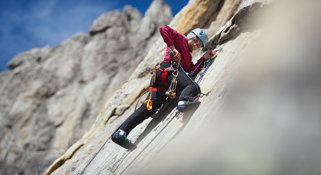 Young woman climber selects tools while processing the route while on a safety station on a vertical rock wall in the mountains, close-up, panorama.
