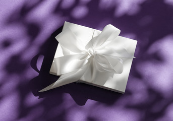 Luxury holiday white gift box with silk ribbon and bow on violet background, luxe wedding or...