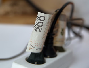 200 Polish zloty banknote between wires of plugs in electric extension cord close up on concept of costs of electricty / recompense of high costs of energy