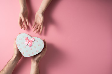 Valentine's Day celebration concept. A nice gift from a loved one. Box with a bow hands of a man and a woman on a delicate pink background. Copy space. Flat lay.