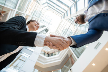 Below view of successful business partners in suits making handshake against panorama of office center