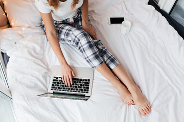 Overhead portrait of woman in checkered pants using laptop. Indoor photo of female freelancer in...