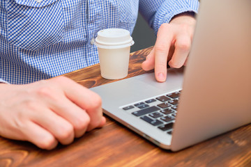 A man works behind a laptop on a wooden table with an hour of espresso.
