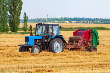 Fototapeta na wymiar A tractor with a trailed bale making machine collects straw rolls in the field and makes round large bales