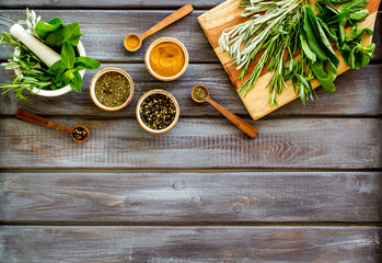 Making spices. Herbs in motar and dry flavorings on dark wooden desk top-down copy space