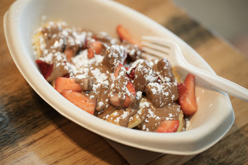 poffertjes with chocolate, strawberries and powdered sugar in a paper bowl with a plastic fork