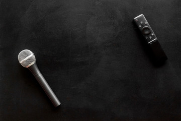 Naklejka premium TV news concept. TV remote and microphone on black background top-down copy space