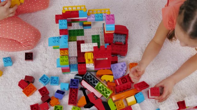Top view: children play plastic constructor sitting on a carpet in kindergarten. Children having fun playing colorful blocks building blocks, education toys.
