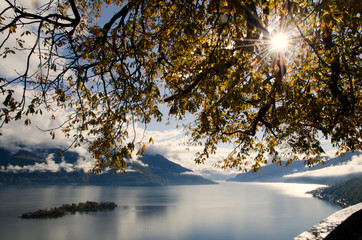 Brissago Islands on Alpine Lake Maggiore in Autumn with Mountain and Tree Branches with Sunbeam in Ticino, Switzerland.