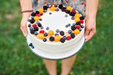 Midsection of woman holding birthday cake outdoors in garden in summer.