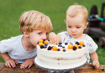 Two toddler children with birthday cake outdoors in garden in summer.
