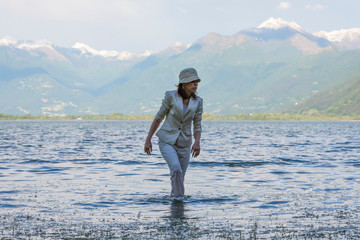 Fototapeta na wymiar Woman Standing in a Flooding Alpine Lake with Snow-capped Mountain in Locarno, Switzerland.