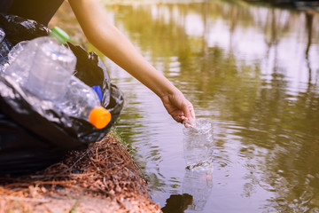 Woman volunteer picking up a bottle plastic trash in river,Environment concept