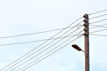 Electric pole with street lamp and wires against blue sky background. Copy space is on the left...