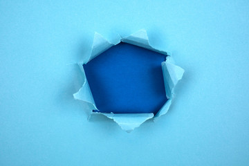 Torn round hole in cyan blue paper with torn edges and a blue background. Space for message, paper texture.