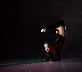 Young girl gymnast in black sport body and uppers lying on floor on neck with streched back and...