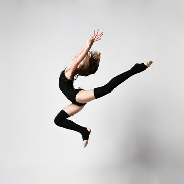 Young girl gymnast in black sport body and uppers jumping and making dymnastic pose in air over white background