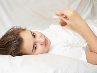 Obraz na płótnie Canvas sick girl lying in white bed with a thermometer in hands. coronavirus