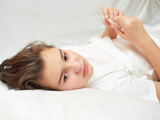 Fototapeta na wymiar sick girl lying in white bed with a thermometer in hands. coronavirus