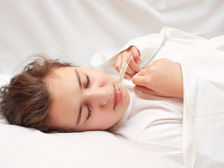 Obraz na płótnie Canvas sick girl lying in white bed with a thermometer in mouth. coronavirus