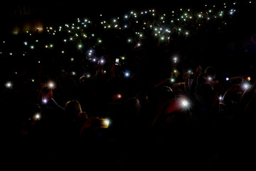 Crowd of people in unfocus holding lights of mobile phones