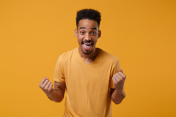 Joyful young african american guy in casual t-shirt posing isolated on yellow orange wall background, studio portrait. People emotions lifestyle concept. Mock up copy space. Doing winner gesture.