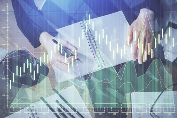 Forex chart hologram on hand taking notes background. Concept of analysis. Multi exposure