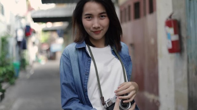 Beautiful smiling young woman traveler looking at camera and use film camera take photos enjoying traveling on holiday summer. Solo travel concept.