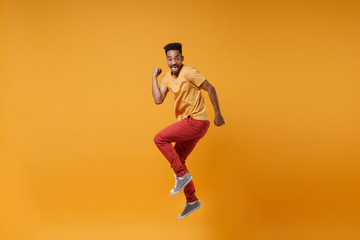 Fototapeta na wymiar Joyful young african american guy in casual clothes posing isolated on yellow orange wall background studio portrait. People lifestyle concept. Mock up copy space. Jumping clenching fists like winner.