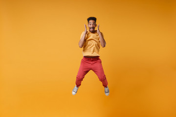 Obraz na płótnie Canvas Excited young african american guy in casual clothes posing isolated on yellow orange wall background studio portrait. People lifestyle concept. Mock up copy space. Jumping keeping hands near face.
