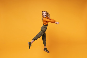 Fototapeta na wymiar Side view of little kid girl 12-13 years old in turtleneck, jumpsuit isolated on orange yellow background children portrait. Childhood lifestyle concept. Mock up copy space. Jumping, looking camera.