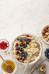 healthy breakfast. Woman eating oatmeal porridge with fresh berry, nuts and honey, top view
