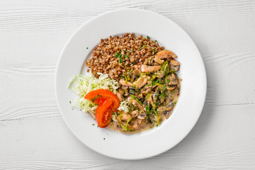 Top view of plate with chicken goulash, mushroom, buckwheat and tomato cabbage salad