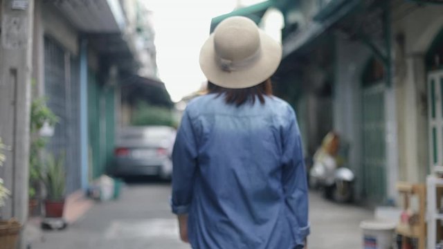 Portrait of young asian woman traveler wearing retro fedora hat walking a small street in Bangkok Thailand. Enjoying traveling on vacation summer. Solo travel concept.