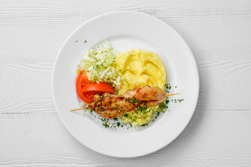 Top view of plate with chicken shashlik, mashed potato and cabbage salad