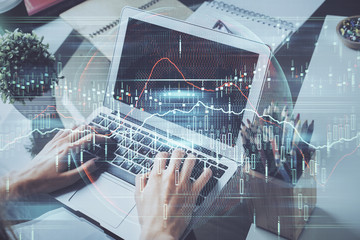 Double exposure of stock graph with businessman typing on computer in office on background. Concept of hard work.