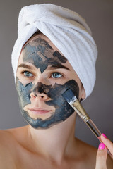 Young woman apply clay facial mask on gray background. Face peeling mask with charcoal, spa beauty treatment, skincare, cosmetology. Close up