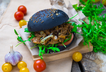 black burger with pork and arugula on a wooden background with garlic and tomatoes