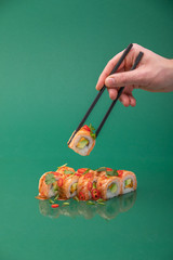 Hand holding sushi roll with chopsticks on green background. set of rolls