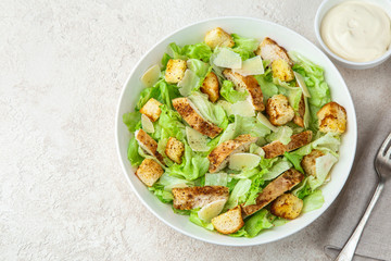 traditional Caesar salad with lettuce, roasted chicken,  croutons and cheese in white bowl