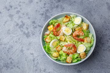 Caesar salad with prawn, roasted chicken,  croutons and cheese in blue bowl