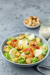 Caesar salad with prawn, roasted chicken,  croutons and cheese in blue bowl