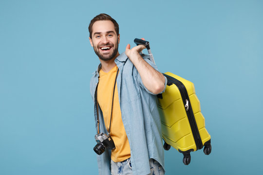 Cheerful traveler tourist man in yellow summer casual clothes with photo camera isolated on blue background. Male passenger traveling abroad on weekends. Air flight journey concept. Holding suitcase.