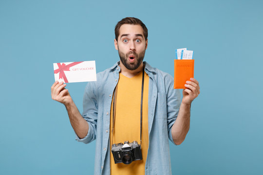 Shocked traveler tourist man in summer clothes with photo camera isolated on blue background. Passenger traveling on weekends. Air flight journey Hold passport boarding pass ticket gift certificate.