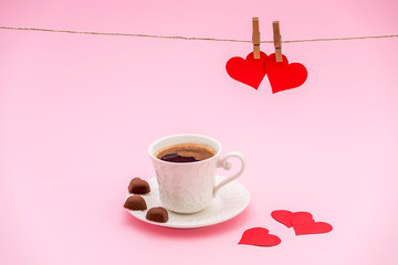 Cup of Coffee grains with heart shaped chocolate cookies and red paper hearts on pink pastel background. Clothes pegs and red paper hearts on rope. Valentines day concept