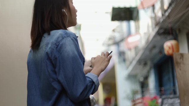 Attractive asian woman using a smartphone finding map at a small street in Bangkok Thailand enjoying South East Asia summer holiday travel vacation.